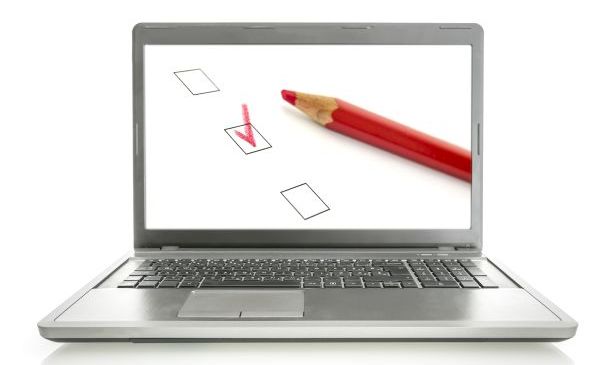 A laptop with a screen displaying a checkbox filled out in red colored pencil, with the red pencil laying next to the checkbox