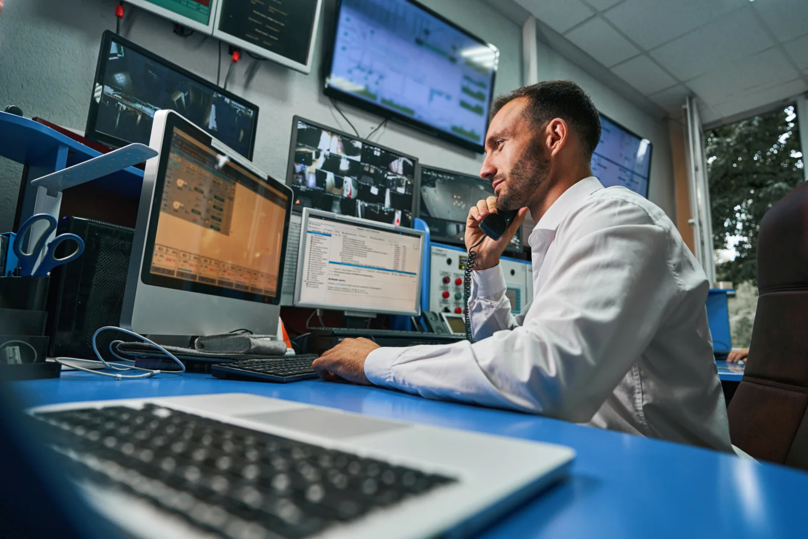 Telehealth operations hub with clinicians using dual-monitor workstations, webcams, and large displays for remote care coordination