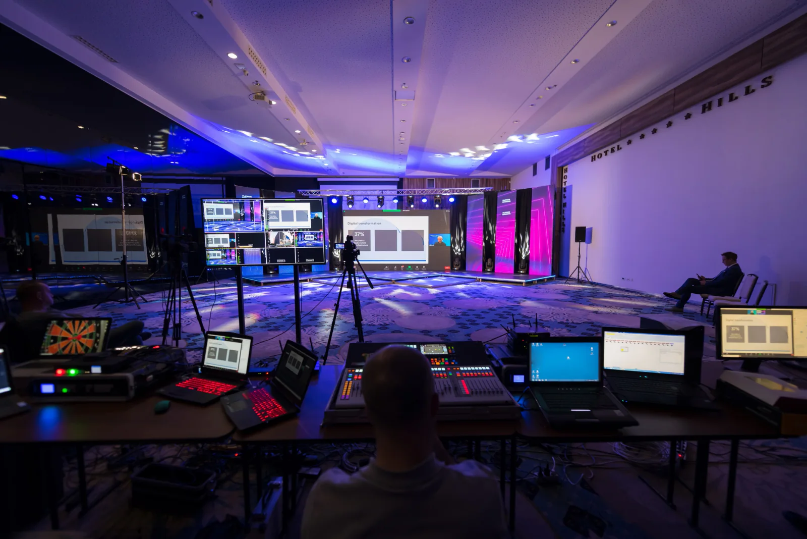 Convention center operations team coordinating overlapping events with laptops, scheduling screens, and floor plans