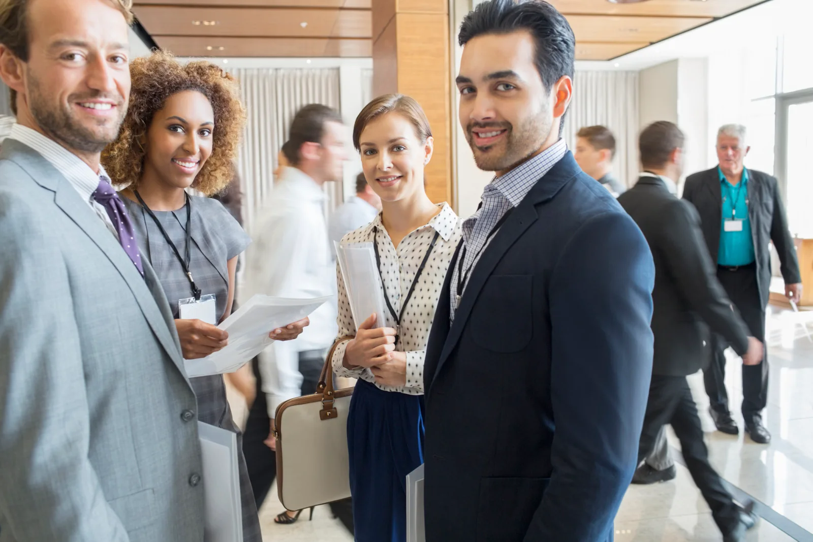 Business professionals networking in a conference venue lobby while wearing event badges