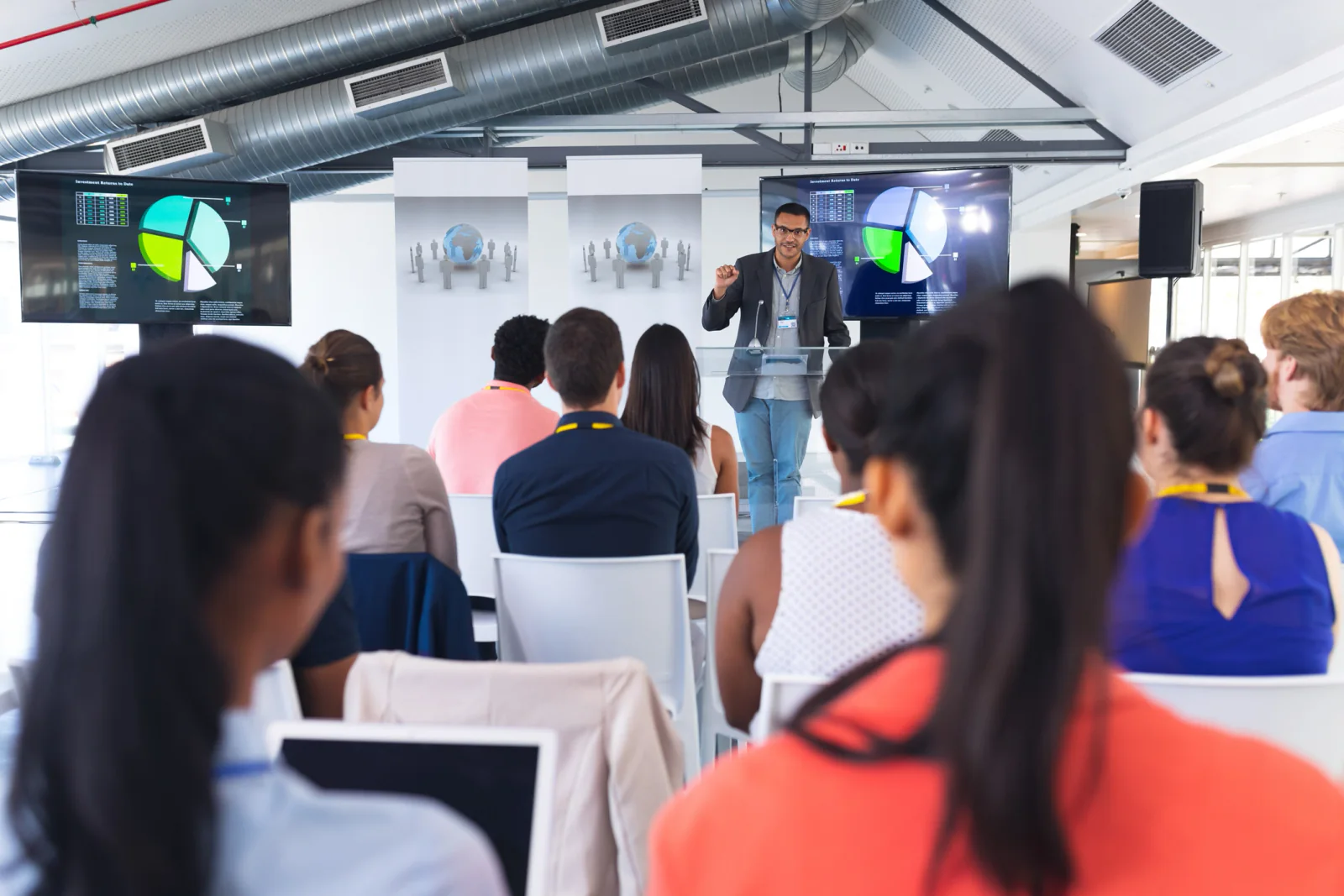 Corporate training room with employees using laptops while a presenter teaches from the front of the room