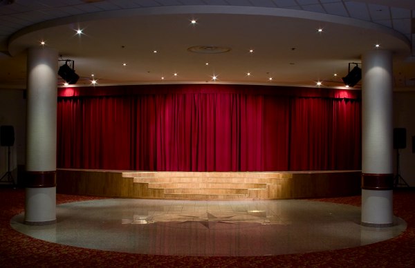 An empty, well lit stage with red drape behind it
