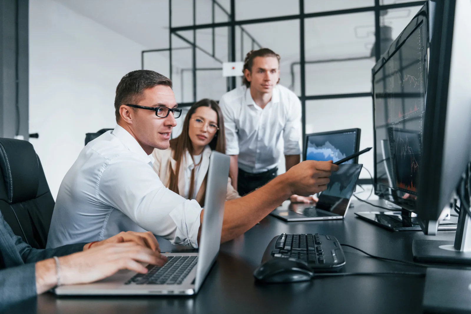 Project coordinator leading a technology deployment meeting with stakeholders, schedules, laptops, and planning documents in a business setting