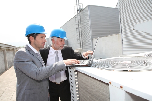 Gas & Oil Industry Rentals Two mean wearing hardhats point at a laptop screen while standing on the roof of a building