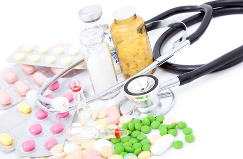 Various medicinal pills and bottles lay next to a stethoscope