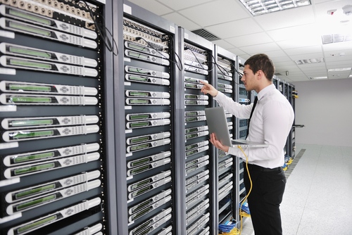 An IT technician with a laptop plugged into a server