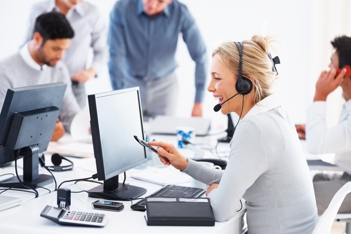 A busy call center with a blond woman wearing a headset while working at a computer