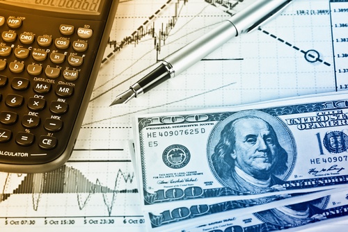 A calculator, pen, and American currency laying on top of financial charts