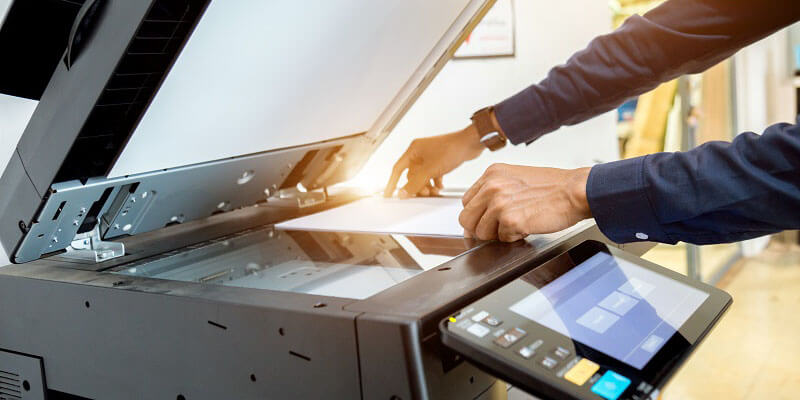 An individual placing a document onto a flat bed copy machine