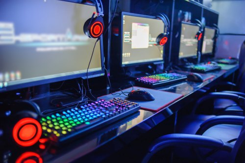 A row of gaming desktops, monitors, mice, chairs, and gaming headsets powered on and boasting LED RGB lighting