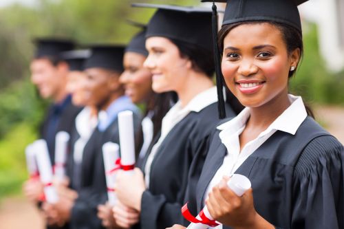 A line of recent graduates wearing their caps and gowns while holding diplomas