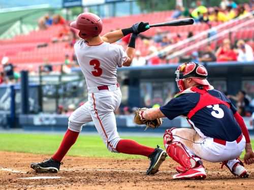 A batter takes a swing at a baseball while the catcher crouches behind home plate