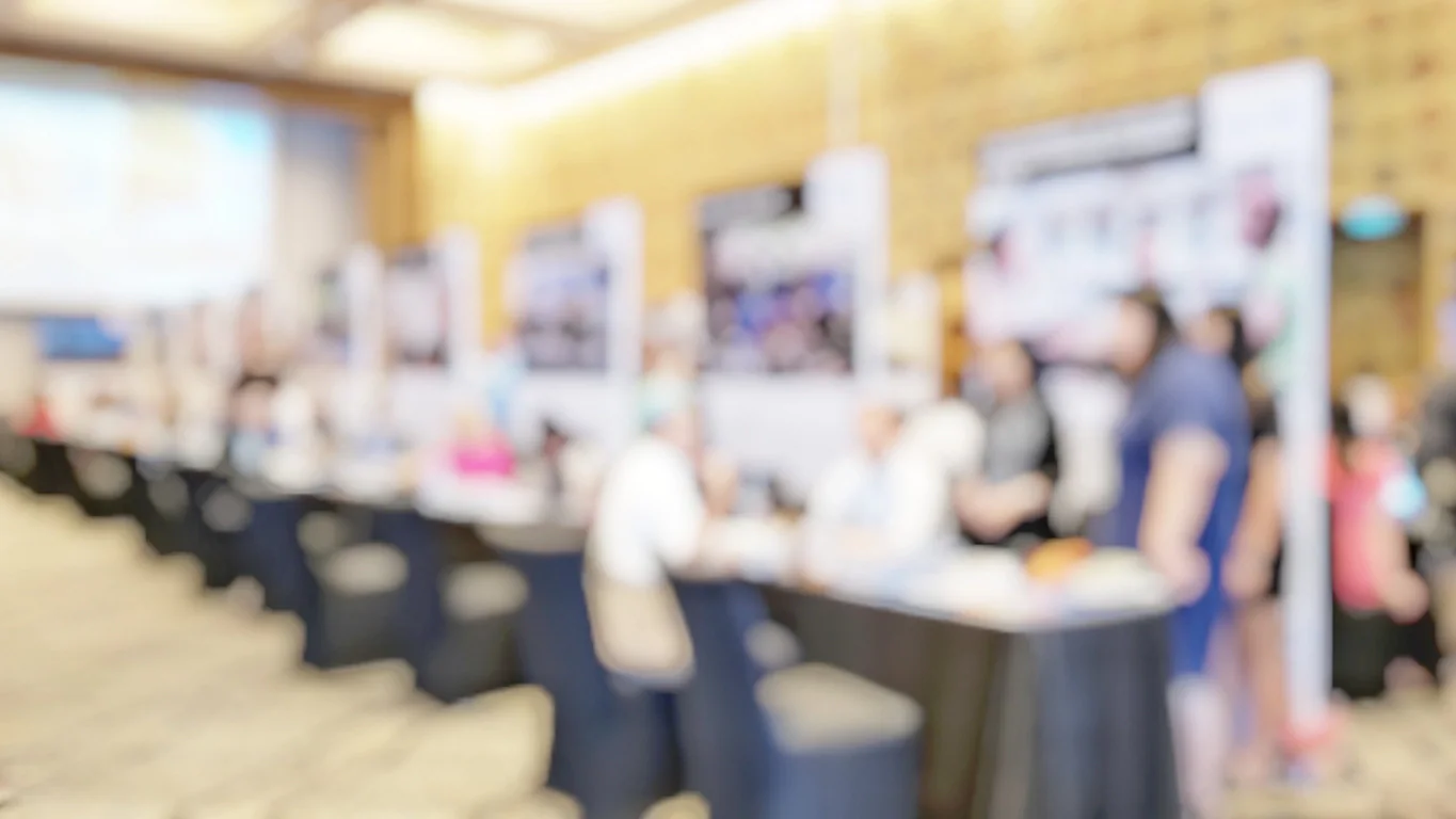 Media event or screening registration area with check-in tablets, large displays, projector setup, and press attendees arriving