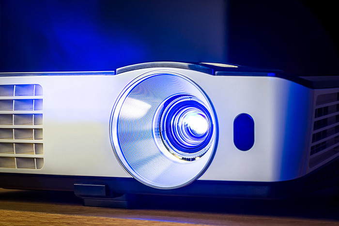 A closer view of a projector in a dark room with the projector bulb illuminated