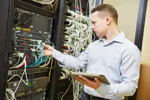 A man plugging ethernet cables into a large switch for server maintenance