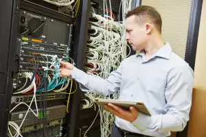 Software Services A man plugging ethernet cables into a large switch for server maintenance