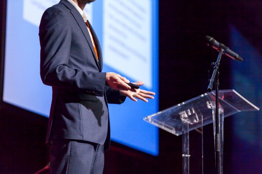 A speaker on a stage in front of a podium with a microphone