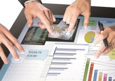 Touchscreen TV Rentals two pairs of hands collaborating on a touchscreen displaying charts of various data