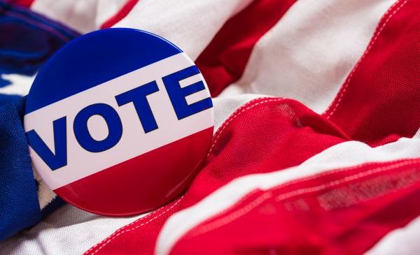 A button encouraging others to vote lays ontop of an American Flag